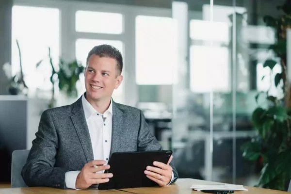 Mann lächelt am Schreibtisch sitzend bei einem Shooting mit Corporate Fotograf in München.
